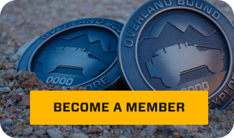 Two Overland Bound emblems in desert sand.